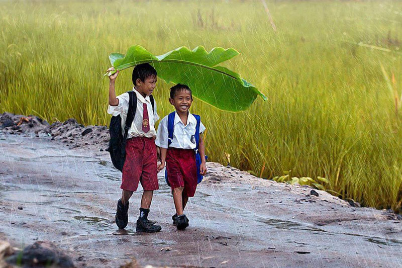 two-kids-under-a-banana-leaf-in-the-rain-indonesia.jpg
